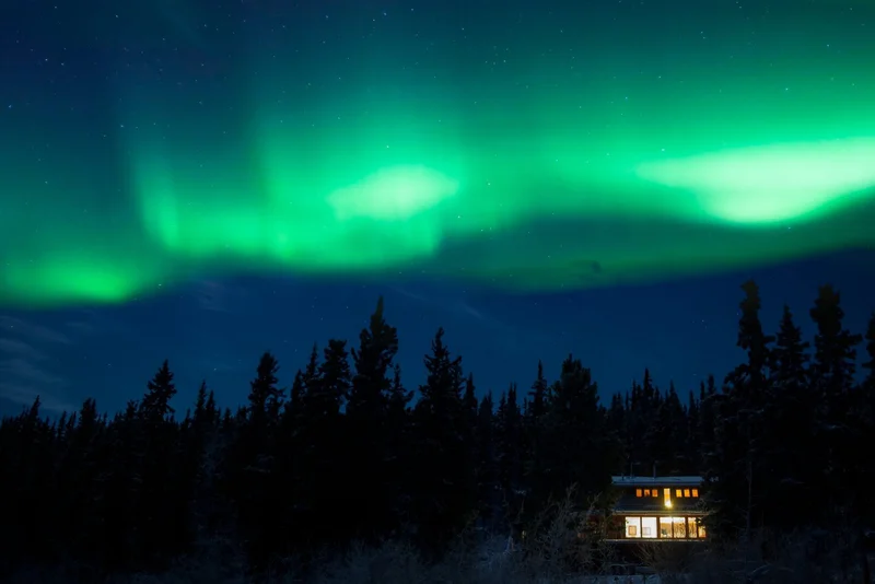 Aurora boreal sobre uma floresta e uma casa